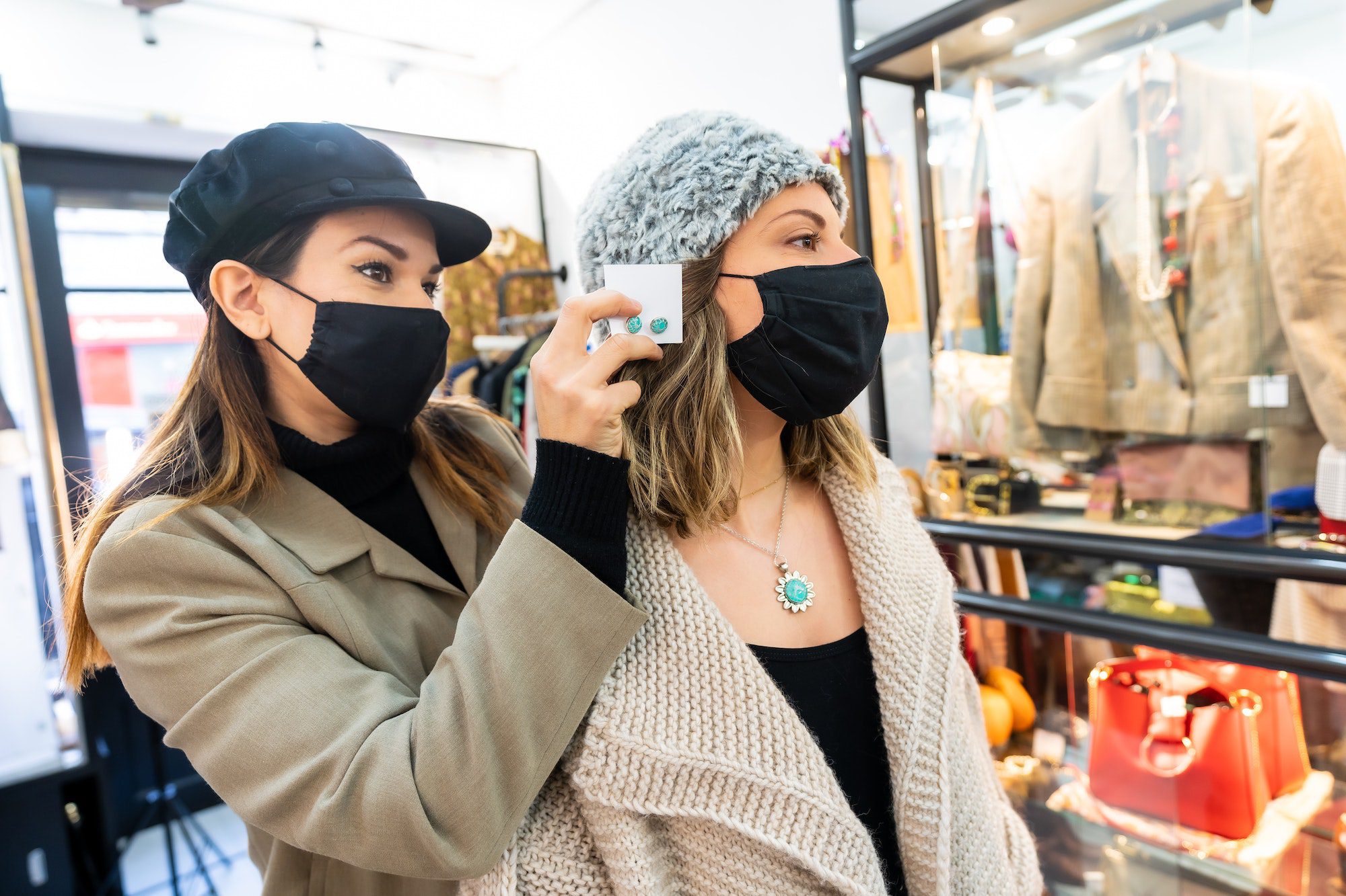 Employee with a mask in a clothing store trying on a jewel to a client, working with